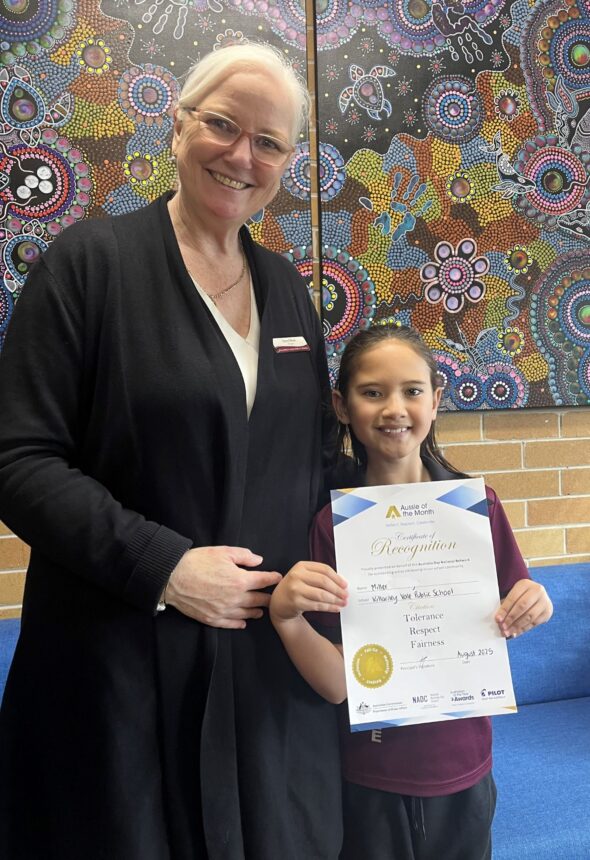 student and principal smiling to camera. The student is holding up a certificate.