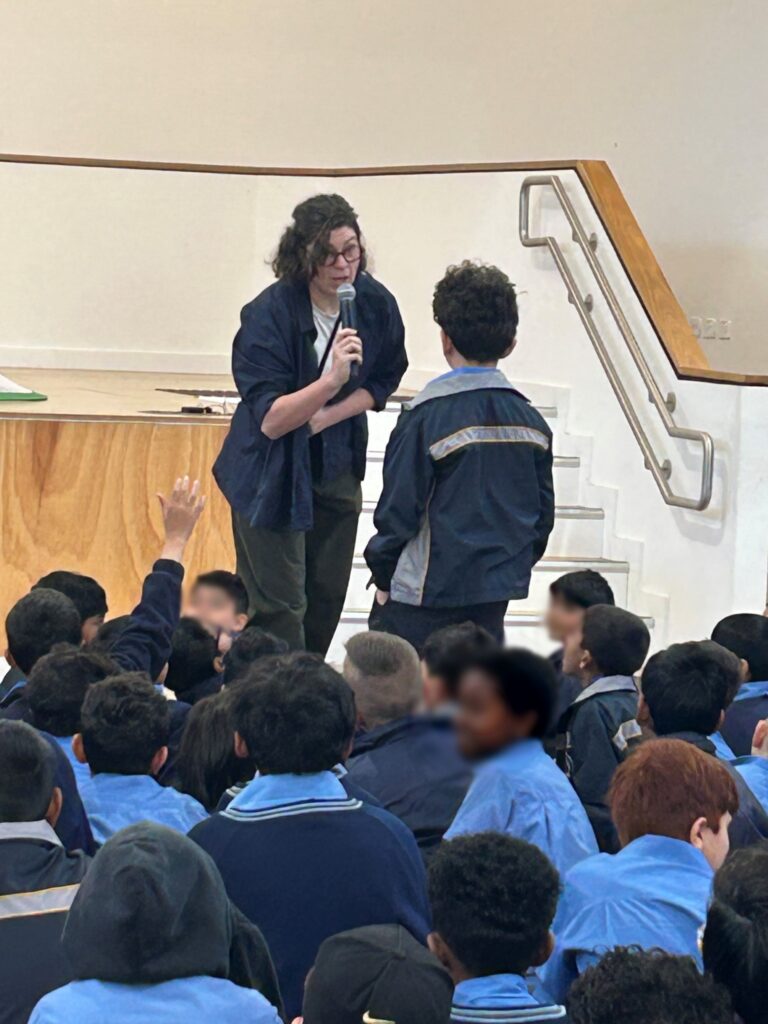 Hannah Costello holding microphone and speaking to young male student with other students sitting around him