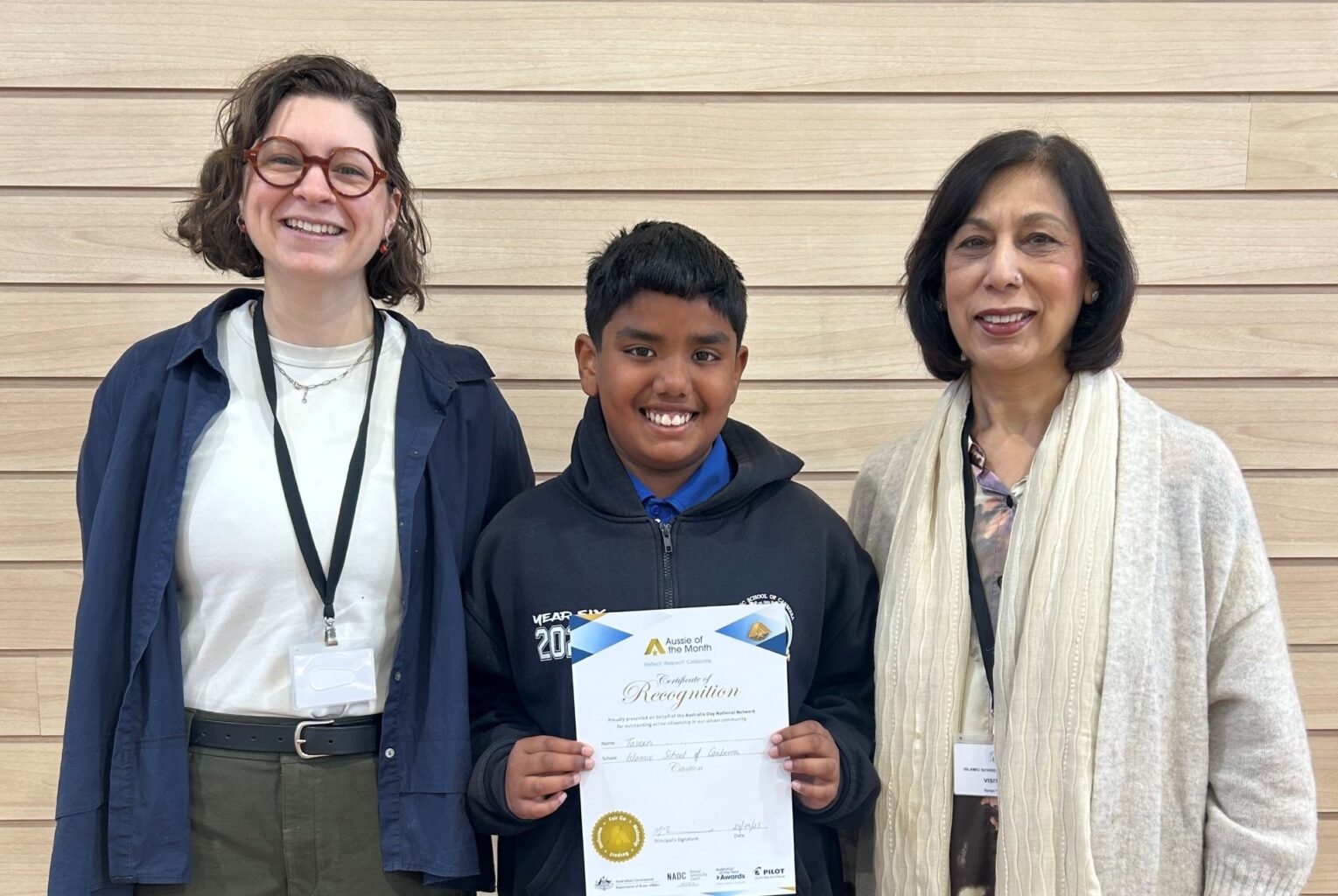 boy holding certificate and smiling with two women standing either side of him