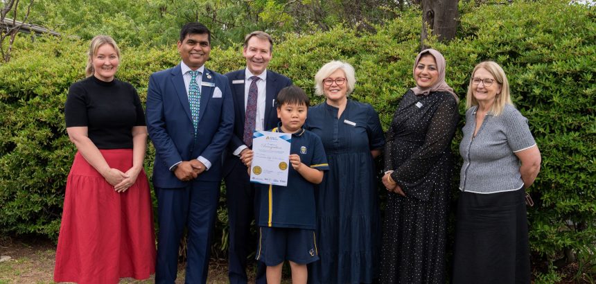 group of adults standing around primary school student holding certificate and smiling to camera